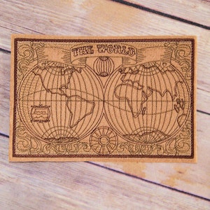 May include: A brown leather patch with a stitched design of a world map. The map is surrounded by a decorative border and the text "THE WORLD" is stitched above the map.