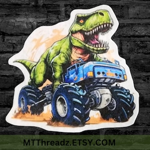 May include: A sticker featuring a green Tyrannosaurus Rex driving a blue monster truck. The dinosaur has an open mouth and orange eyes. The truck has large, dark blue tires. The text "MTThreadz.ETSY.COM" is at the bottom.