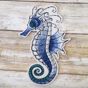 May include: Blue and green embroidered seahorse patch with a white background. The seahorse has a detailed design with swirls and a curled tail.