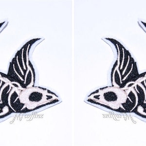 May include: Two identical black and white patches in the shape of a bird skeleton. The patches have a white outline and are on a white background. The text "Mj coffinz" is written in cursive at the bottom of each patch.