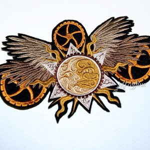 May include: Embroidered patch featuring a stylised sun with gears and wings. The sun is gold and white, the gears are black and orange, and the wings are brown and beige.