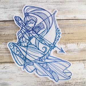 May include: Blue and white embroidered design of a woman with a bow and arrow. The design is on a white felt background.