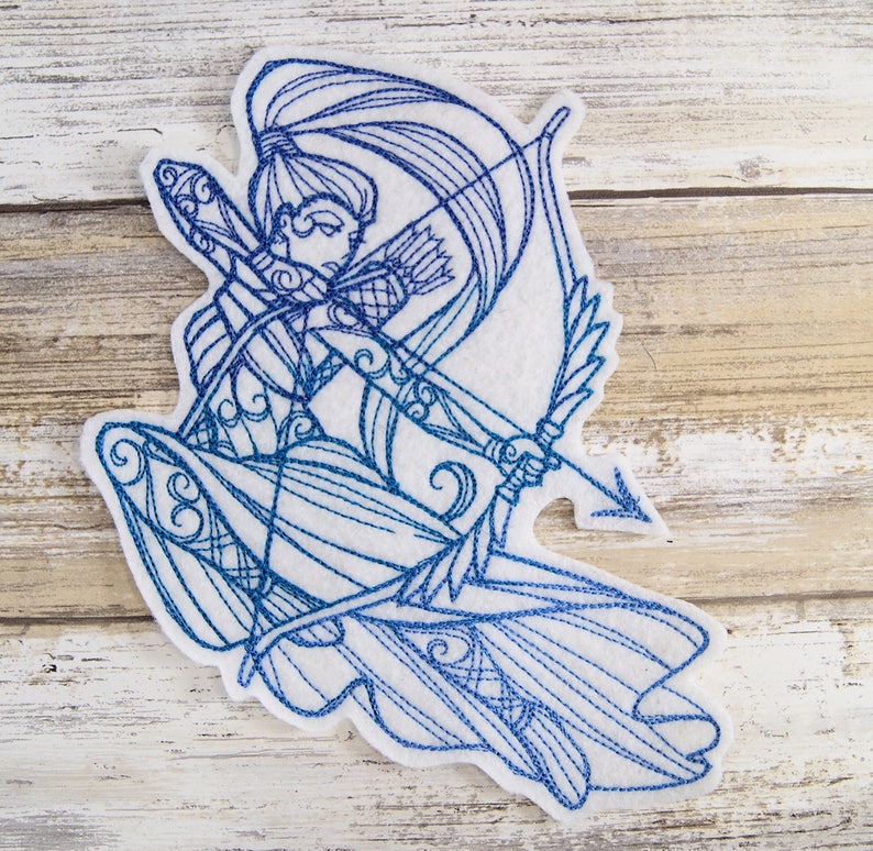 May include: Blue and white embroidered design of a woman with a bow and arrow. The design is on a white felt background.