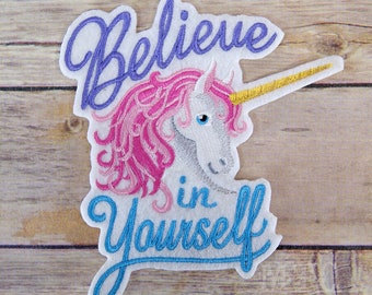 May include: White embroidered patch with a pink unicorn and a gold horn. The unicorn has a blue eye and a pink mane. The text "Believe in Yourself" is embroidered in blue.