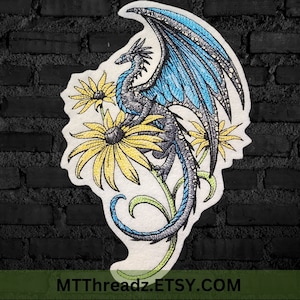 May include: Embroidered design of a blue and black dragon with wings spread, perched on a stem with yellow flowers. The design is on a white background.