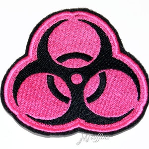 May include: An embroidered patch featuring a pink and black biohazard symbol. The symbol is a stylised triangle with three circles, each containing a black line.