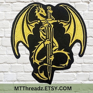 May include: Black patch with a gold embroidered dragon holding a sword. The dragon has large wings and is centered on the patch. The text "MTThreadz.ETSY.COM" is at the bottom of the patch.