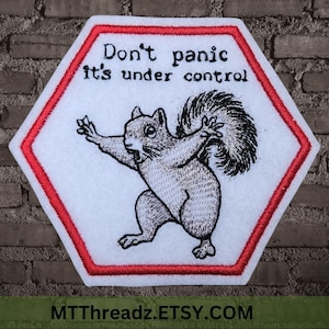 May include: A white hexagonal patch with a red border. The patch features a black and white embroidered image of a squirrel with the text "Don't panic it's under control".