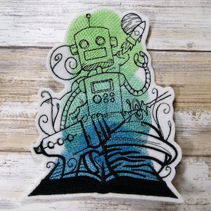 May include: Embroidered patch featuring a green robot holding a rocket, standing on a blue and green book with swirling designs. The robot has a large head with two eyes and a small mouth.