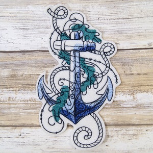 May include: An embroidered patch featuring a blue anchor with white rope and green seaweed details. The anchor is surrounded by a white background.