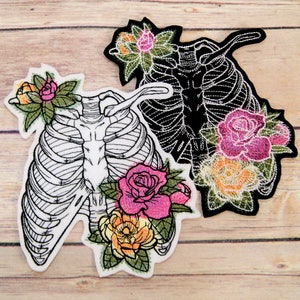 Peut inclure: Deux patchs brodés représentant une cage thoracique avec des accents floraux. Un patch est blanc avec des contours noirs et l'autre est noir avec des contours blancs. Les deux patchs présentent des fleurs roses, jaunes et vertes.