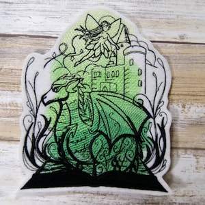 May include: Embroidered patch featuring a green dragon with wings, a fairy flying above a castle, and black floral details.