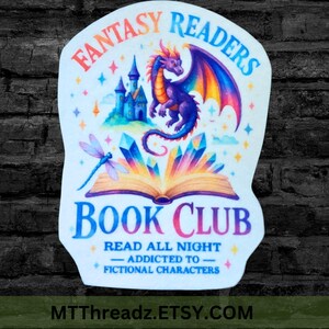 May include: A sticker with the text "Fantasy Readers Book Club" featuring a dragon, castle, and open book with crystals. The design includes a dragonfly and the phrase "Read All Night - Addicted to Fictional Characters."
