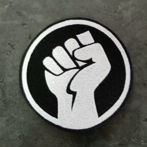 May include: A white raised fist in a black circle, a symbol of protest and solidarity.