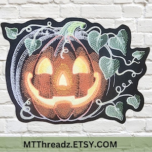 May include: An embroidered patch featuring a glowing orange jack-o'-lantern with a wide, toothless grin and triangular eyes. The pumpkin is surrounded by green embroidered vines and heart-shaped leaves on a black background. Text reads MTTHREADZ.ETSY.COM.