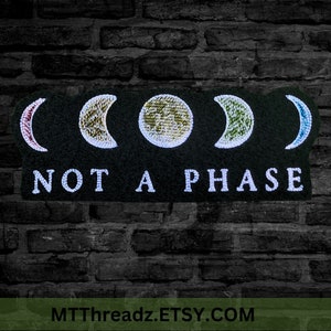 May include: Black felt patch with four embroidered moon phases in different colors and the text "NOT A PHASE" in white.