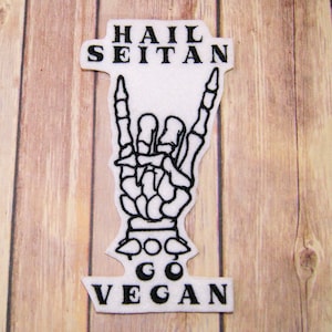 Peut inclure: Patch blanc avec du texte brodé noir "Hail Seitan" et "Go Vegan" avec une main de squelette noire faisant le signe rock and roll entre les deux.