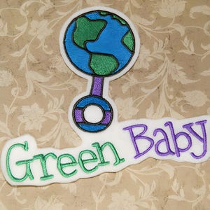 May include: Green Baby embroidered patch featuring a purple and blue rattle shaped like a globe. The globe has green continents and a blue ocean.