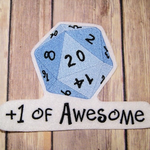 May include: A blue and white embroidered patch of a twenty-sided die with the numbers 1 through 20. The patch has the text " +1 of Awesome" below the die.