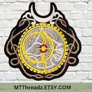 May include: Embroidered patch featuring a circular design with a crescent moon, snakes, and a compass-like symbol in the center. The patch is on a white brick background.