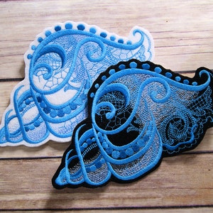 May include: Two embroidered patches with a blue and white lace design. The patches are on a wooden surface.