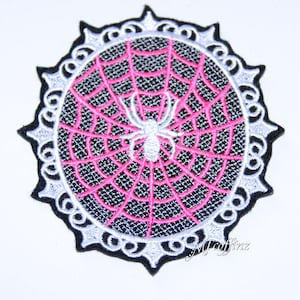 May include: A white spider embroidered on a pink spiderweb in a white and black circular frame.