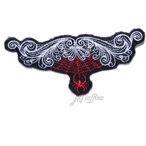 May include: Black and white embroidered patch with a red spider's web and a red spider in the centre. The patch has a decorative design around the edges.