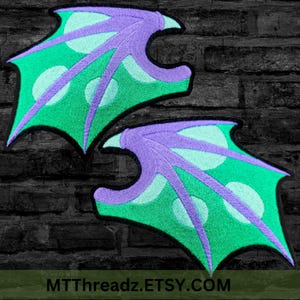 May include: Two green and purple dragon wings with a black outline. The wings have a polka dot pattern.