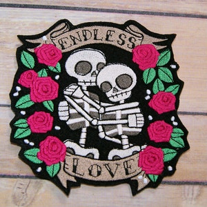 May include: Embroidered patch featuring two skeletons embracing, surrounded by pink roses and green leaves. The banner above reads "ENDLESS" and the banner below reads "LOVE".