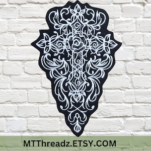 May include: A black fabric patch with a white embroidered design of a cross with a rose in the center and intricate floral details. The patch is shaped like a teardrop.