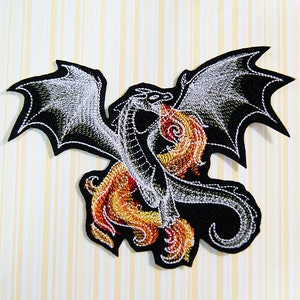 May include: Embroidered iron-on patch featuring a black dragon with silver wings and a tail engulfed in orange and yellow flames.