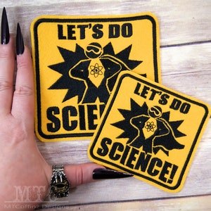 May include: Two yellow and black embroidered iron-on patches with the text "Let's Do Science!" and a cartoon image of a person in a superhero pose with an atom symbol on their chest.