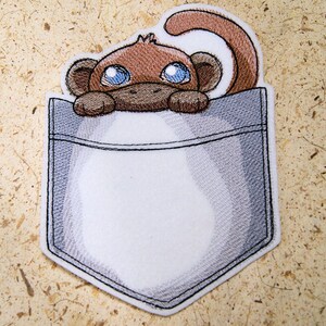 May include: Embroidered patch of a brown monkey peeking out of a gray pocket. The monkey has large blue eyes and a brown nose.