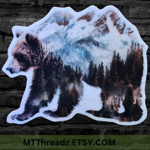 May include: A brown bear silhouette with a snowy mountain range and a forest scene layered over it. The image is a watercolor style illustration.