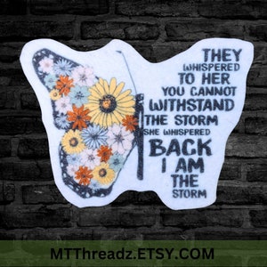 May include: A white sticker with a butterfly design and the text "They whispered to her you cannot withstand the storm she whispered back I am the storm".