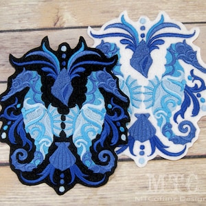May include: Two blue and white embroidered seahorse designs with a shell and floral accents. The designs are on black and white fabric.