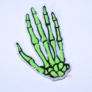 May include: An embroidered patch of a neon green skeleton hand with black detailing and a white border. The design showcases the bone structure, ideal for Halloween or gothic-inspired crafts.