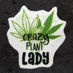 Puede incluir: Parche blanco con ilustraciones de hojas de marihuana verdes y el texto "Crazy Plant Lady".