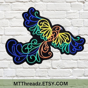 May include: A colorful embroidered patch of a stylized bird with blue, green, yellow, and orange thread. The bird is flying with its wings spread out. The patch is on a white brick background. MTTThreadz.ETSY.COM is written below the patch.