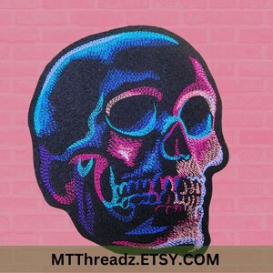 May include: A black embroidered skull patch with blue, pink, and purple details. The skull is facing to the right and has a detailed design.