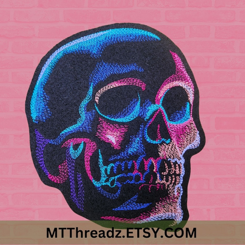May include: A black embroidered skull patch with blue, pink, and purple details. The skull is facing to the right and has a detailed design.