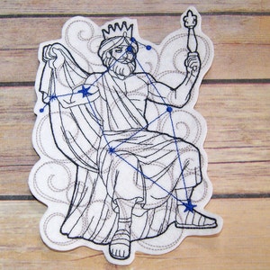 May include: A white felt patch featuring a seated figure with a crown, beard, and staff. The figure is outlined in black stitching, with blue star-shaped accents and connecting lines. The patch has a decorative, cloud-like border.