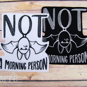 May include: Two embroidered iron-on patches featuring a black bat and the text "NOT A MORNING PERSON". One patch is white with black embroidery and the other is black with white embroidery.