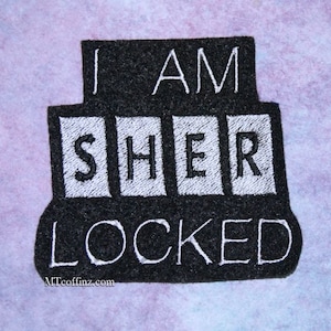 May include: Black and white embroidered patch with the text "I am Sherlock" and "Locked" on a black background.