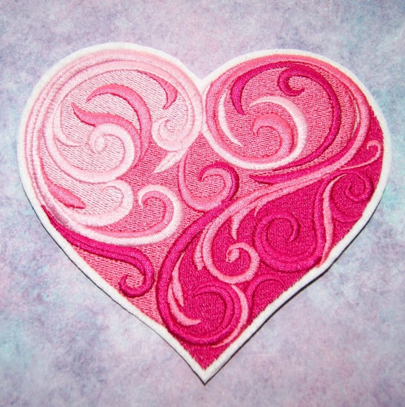 May include: A pink and white embroidered heart-shaped patch with a swirling design.