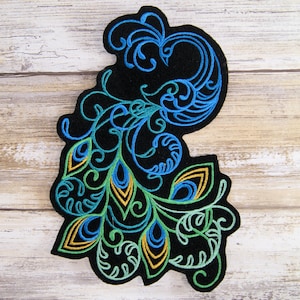 Peut inclure: Un patch en feutre noir avec un motif de paon brodé. Les plumes de la queue du paon sont soulignées de fil bleu, vert et jaune.