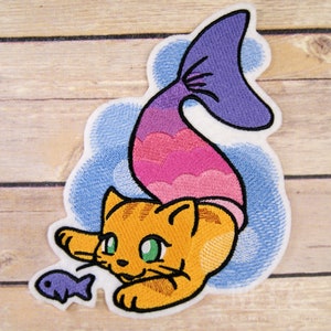 May include: Embroidered iron-on patch of an orange cat with a pink and purple mermaid tail, swimming in blue water and chasing a purple fish.