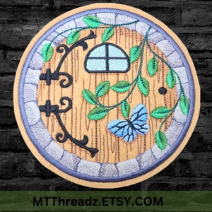 May include: Embroidered patch featuring a round wooden door with a small window, vines, and a blue butterfly. The door has a black metal handle and is surrounded by a gray stone frame.