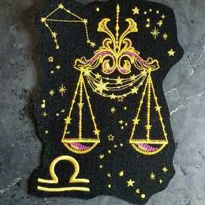 May include: Gold embroidered zodiac patch with a Libra symbol and a constellation design on a black felt background.