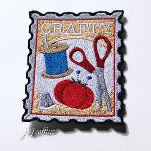 May include: Embroidered patch with a vintage postage stamp design. The patch features the word "CRAFTY" in white lettering, a spool of blue thread, a red pair of scissors, and a red tomato.